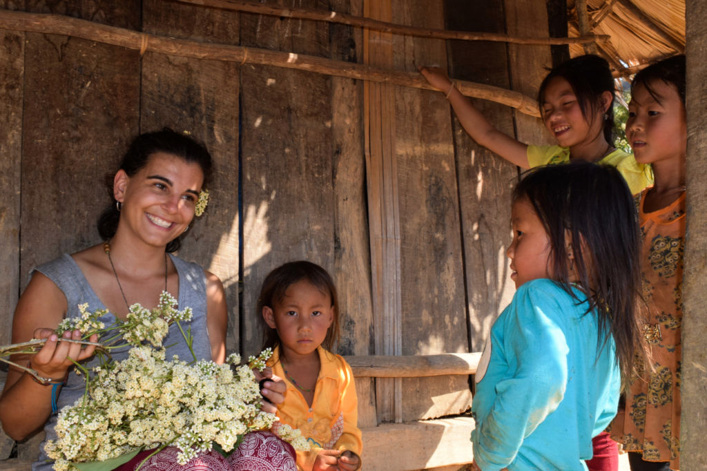 Mujer con flores en la mano y rodeada de niños en una cabaña en Laos