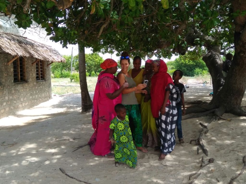 Mujer occidental rodeada de mujeres africanas en un patio exterior y bajo un árbol
