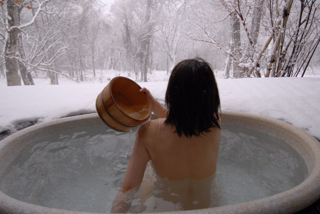 Mujer de espaldas echándose agua en un baño en un onsen japonés